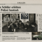 Im Polizeirevier Berlin-Plötzensee sitzen dänische Schüler und Lehrer am Tisch, im Hintergrund prangt das Schild „110“.