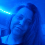 Im blauen Licht blickt Eve in die Kamera, während ihr langes Haar über die Schulter fällt und der Ausdruck nachdenklich wirkt.