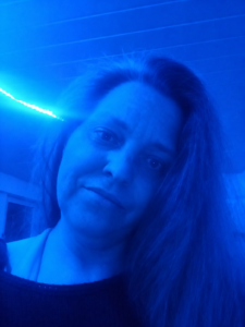 Im blauen Licht blickt Eve in die Kamera, während ihr langes Haar über die Schulter fällt und der Ausdruck nachdenklich wirkt.